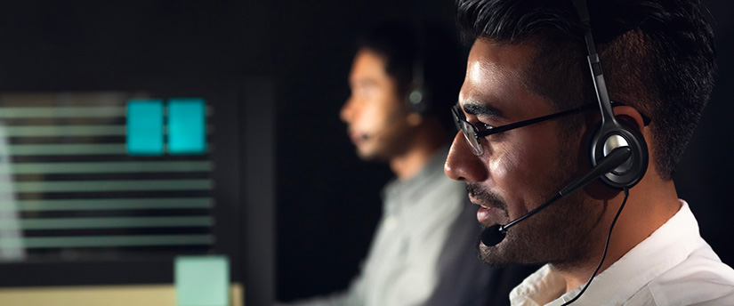 Deux hommes dans un centre d'appel portant des écouteurs, fournissant une assistance à la clientèle pour des courtiers en devises.