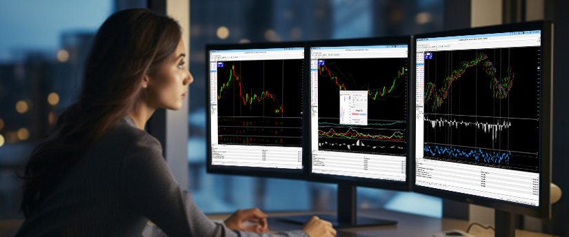 Female trader analyzing USD/SEK forex charts on three computer monitors using trading software in a modern office at night.