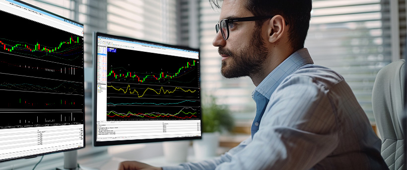 Um homem usando óculos analisa dados de negociação de forex exibidos em dois monitores de computador